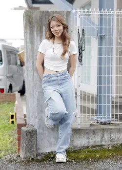 白いクロップトップとダメージデニムを着用し、フェンスに寄りかかっている女性ファッションモデル