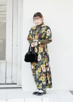 花柄のロングワンピースを着用し、白い壁の前でポーズを取る女性ファッションモデル