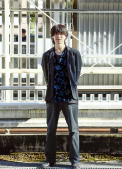 黒のジャケットと青のシャツを着用し、外でポーズを取る男性ファッションモデル