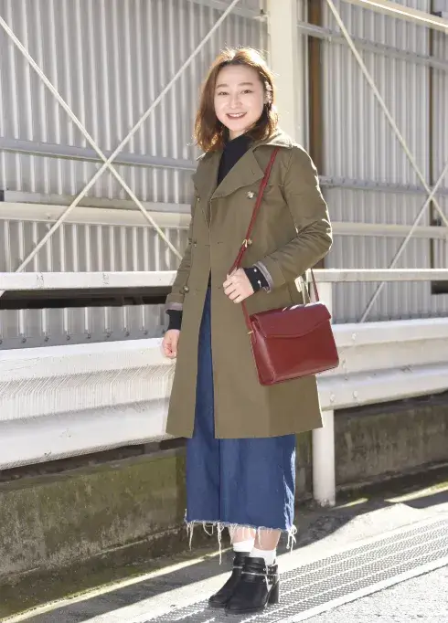 カーキのコートとデニムパンツ、赤いショルダーバッグを身につけた女性ファッションモデル