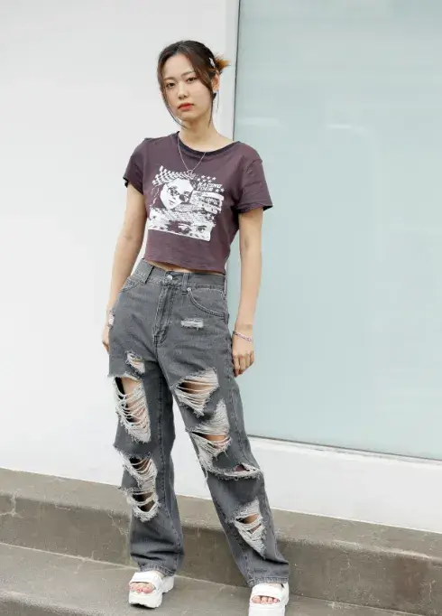 黒いクロップトップとダメージジーンズを着用し、ポーズを取る女性ファッションモデル
